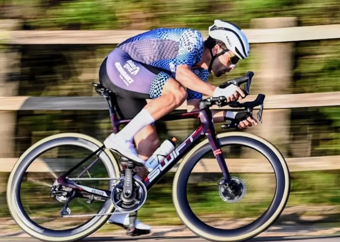 A rider low over the bars at racing speed, the fence behind pulled into a blur