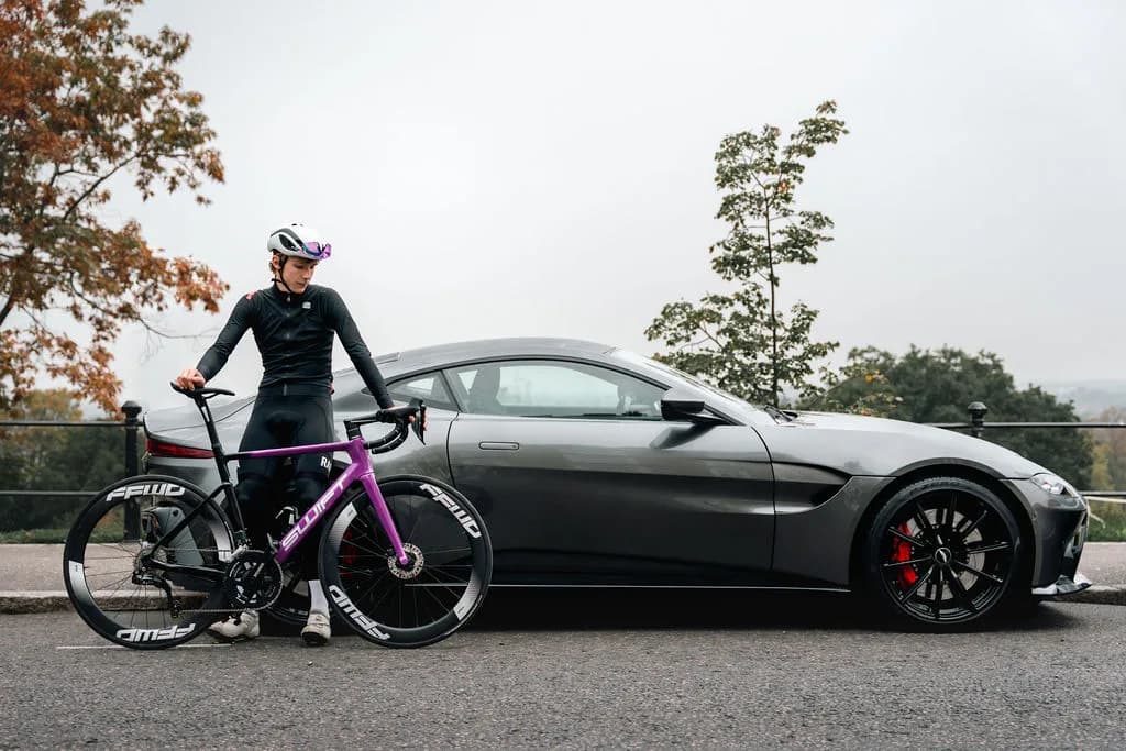 A Swift held at the roadside in front of a sports car, autumn leaves across the tarmac