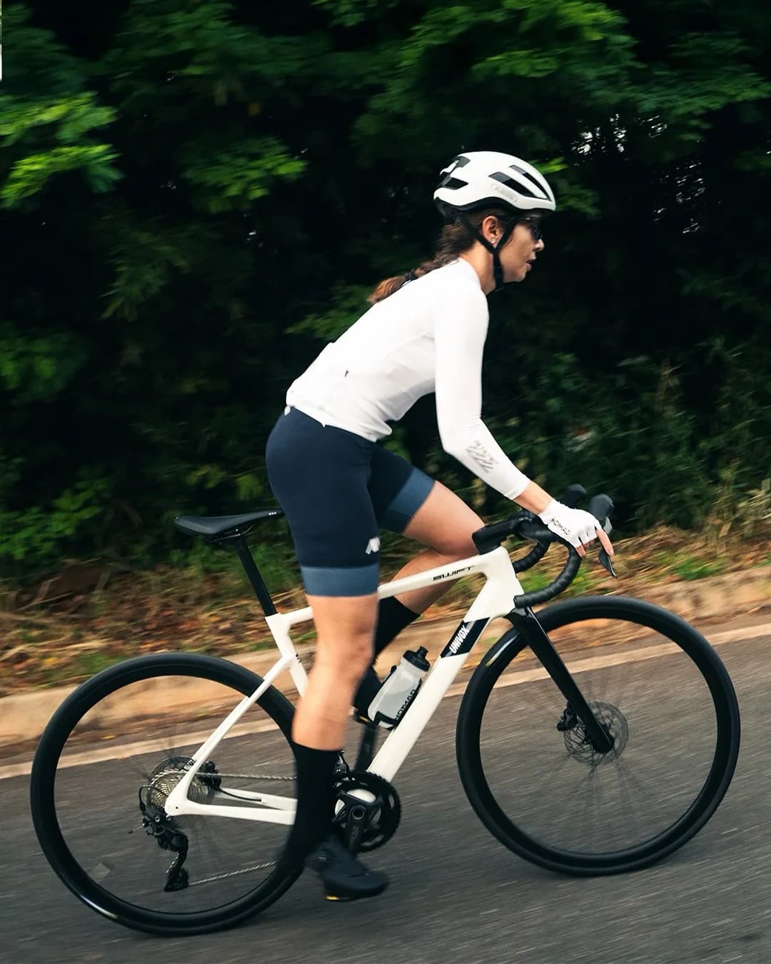A rider carrying speed on a white Swift, the treeline behind pulled into a green blur