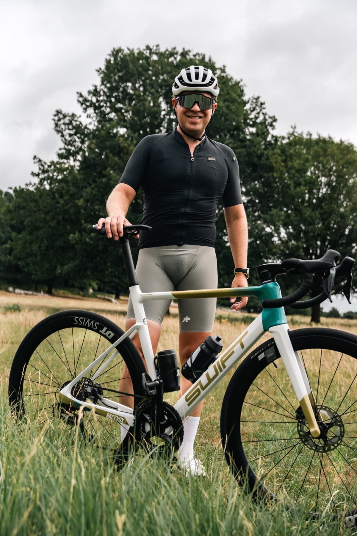 A rider standing with a Swift road bike in the long grass of a Richmond Park meadow